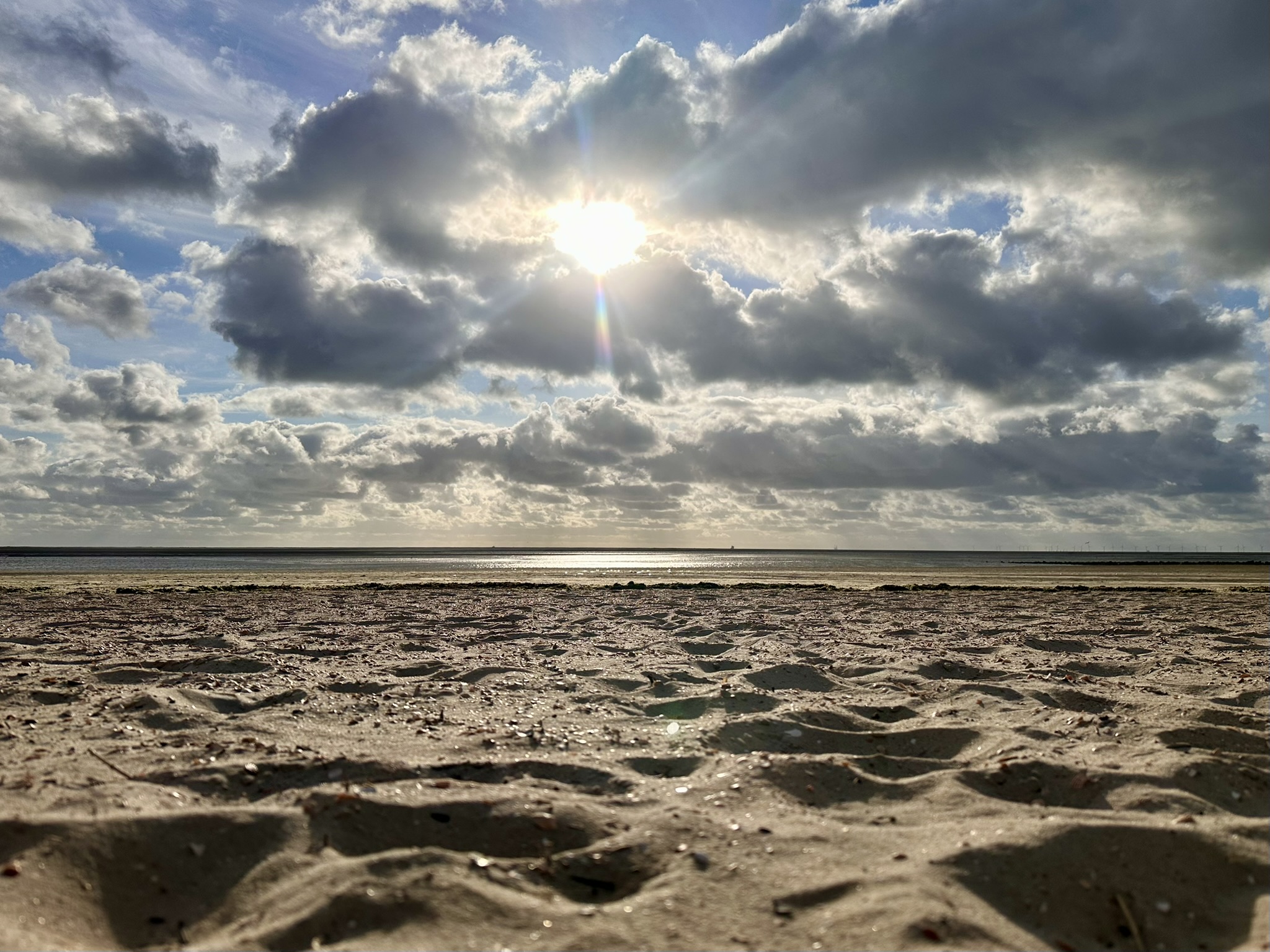 Sonne bricht am weiten Nordseestrand durch die Wolken